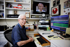 John Miley sits at a desk while working with sports broadcasting media.